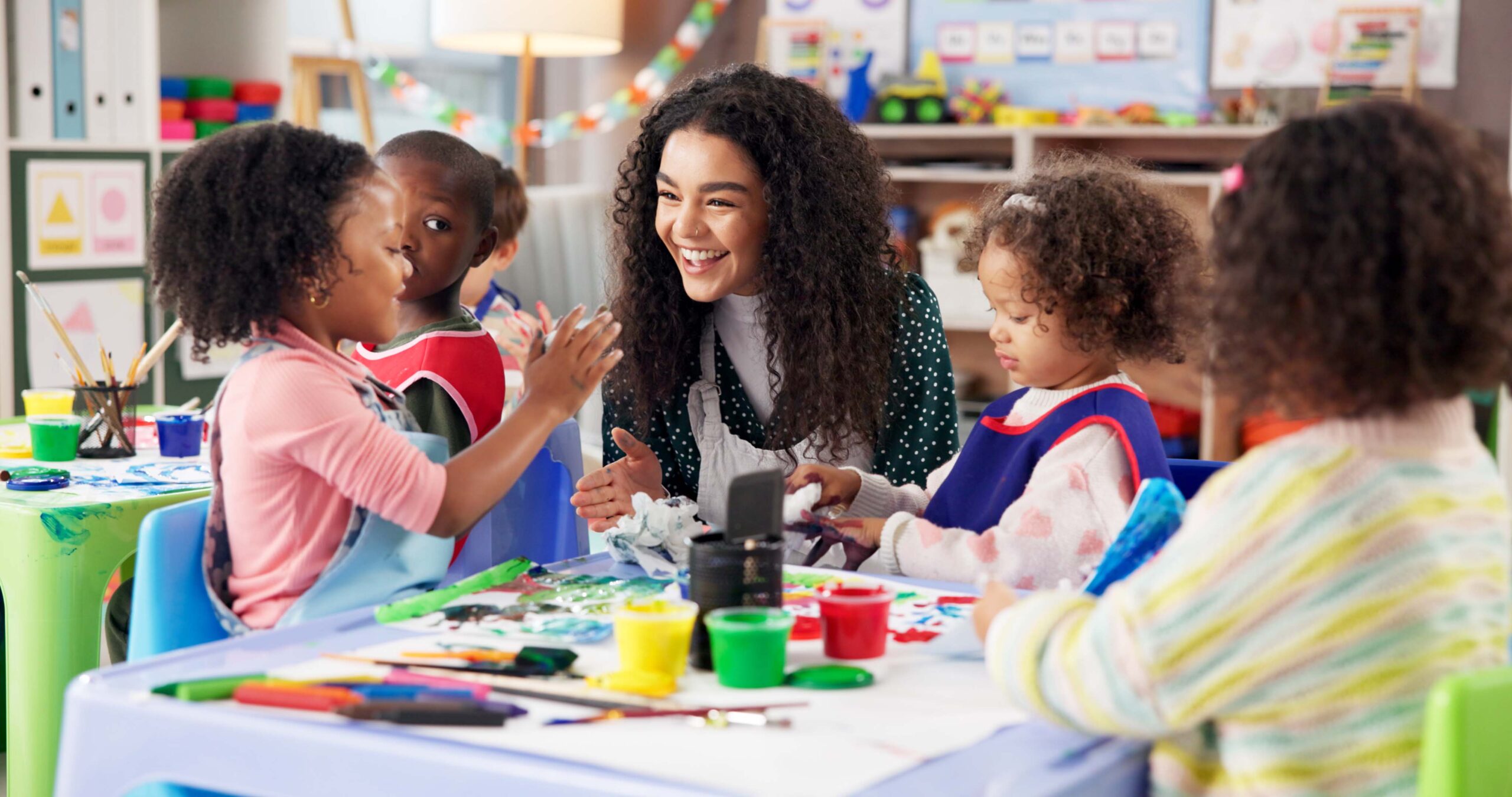 children painting with teacher in class for art, creative talent or motor skill development in preschool. Learning, students drawing or teaching happy kids for lesson or help with color
